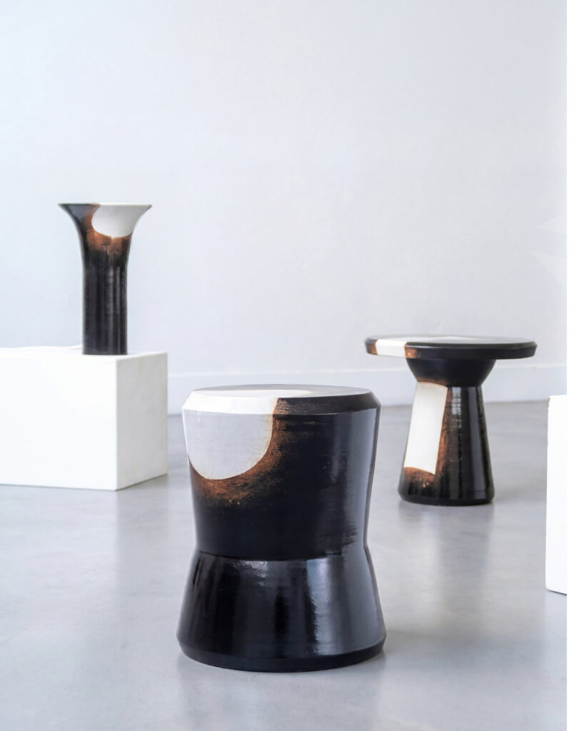 Mobilier et objets en céramique artisanale noire et blanche de la collection Anamorphose : tabouret Georges au premier plan, table basse et vase sur socle en arrière-plan.