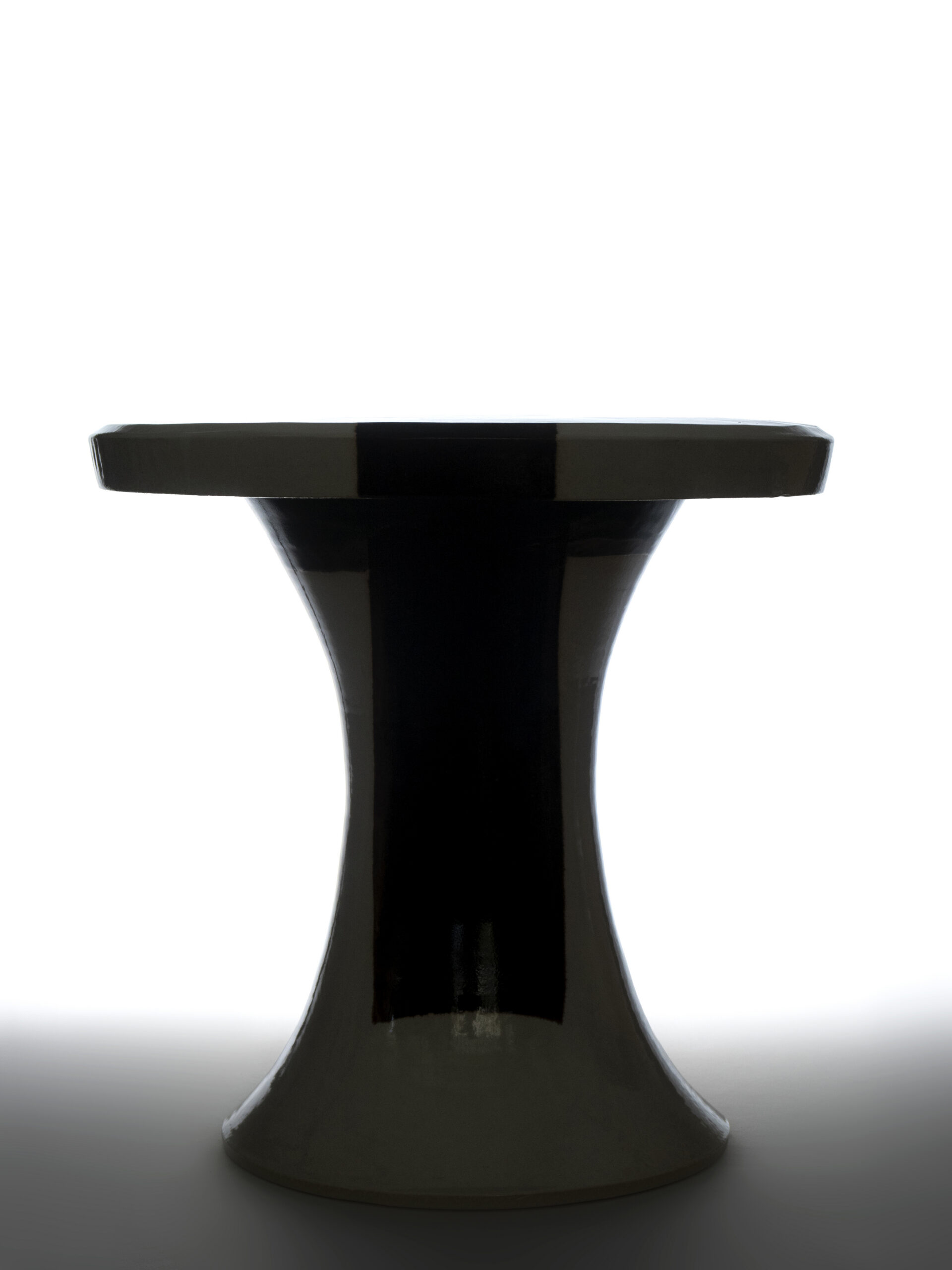 Silhouette en contre-jour d'une table basse ARTHUR en céramique artisanale bicolore au pied évasé.