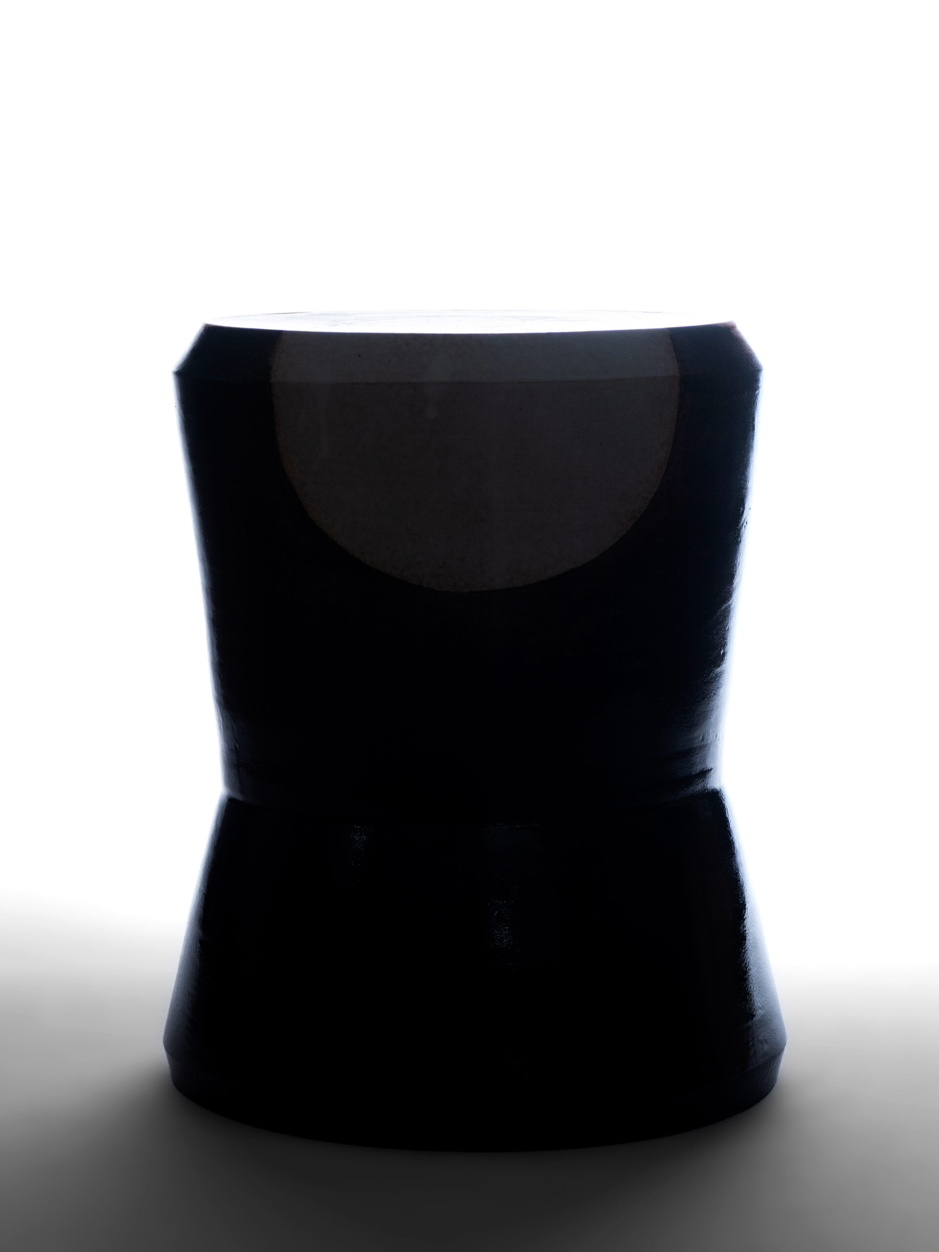 Silhouette rétroéclairée du tabouret Georges en céramique noire et blanche, mettant en valeur sa forme évasée et son motif circulaire.
